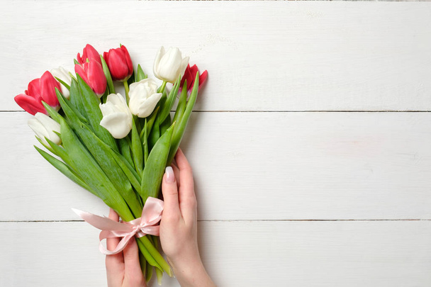 Womans hands holding Bouquet of tulips on white wooden horizontal striped board. Greeting card for International Womans Day, Mothers Day, wedding, birthday, spring holidays. Vintage mockup, copy space - Zdjęcie, obraz