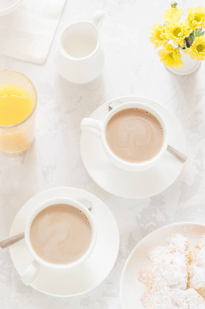 Ontbijt op witte tafel. Koffie of thee met melk, jus d'orange, appeltaart en gele bloemen. Bovenaanzicht - Foto, afbeelding