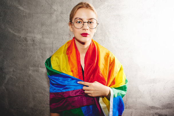 Uma bela jovem com óculos redondos e usando uma bandeira LGBTQ arco-íris. Lésbicas, gays, bissexuais, transgêneros, gays. Homossexual homem
 - Foto, Imagem