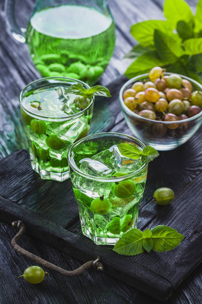 green gooseberry cocktail with ice and fresh mint on a black wooden table. refreshing summer drink - Фото, изображение