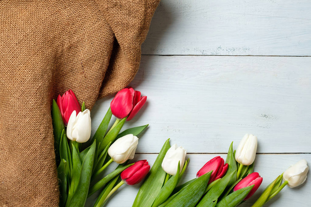 Bunch of tulips and burlap fabric on light blue wooden table. Banner mockup for easter, womans day, mothers day, spring holidays - Foto, afbeelding