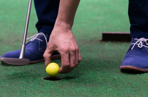 Minigolf speler trekt een gele bal uit het gat, close-up - Foto, afbeelding