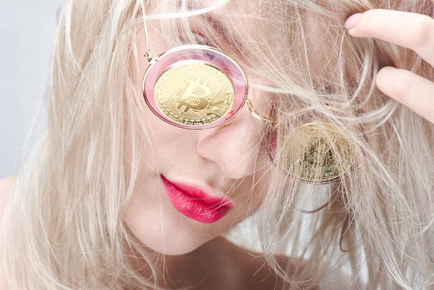 Beautiful young blond woman with red lips in glasses with bitcoins on a white background. Cryptocurrency concept - Fotografie, Obrázek