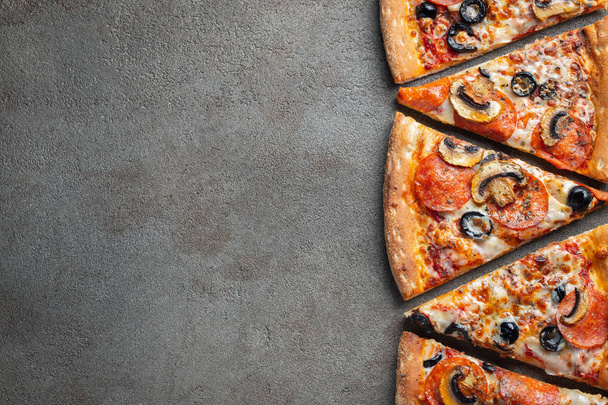 Cut into slices delicious fresh pizza with sausage pepperoni and cheese on a dark background. Top view with copy space for text. Pizza on the black concrete table. flat lay. - Photo, image