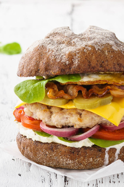 Whole grain cheeseburger with chicken or turkey, lettuce, tomato and bacon. White wooden background. - Foto, Bild