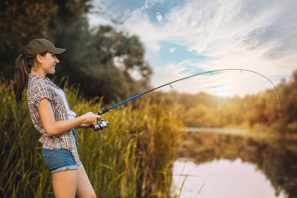 Cute woman is fishing with rod on the summer lake - 写真・画像