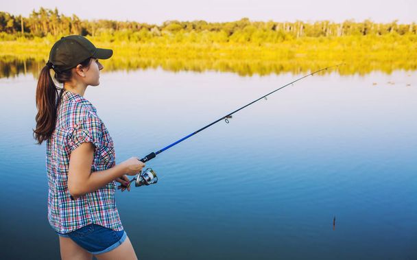 Cute woman is fishing with rod on the summer lake - Fotografie, Obrázek