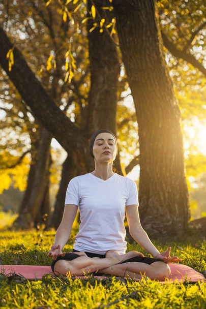 Beautiful young girl meditating in autumn park at sunset - 写真・画像