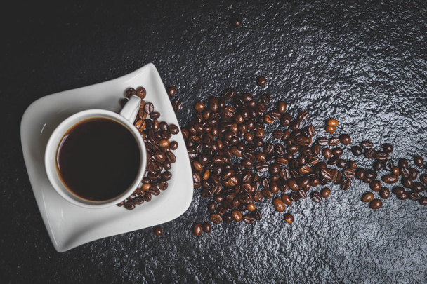 Біла чашка кави і кавових зерен на чорному кам'яному столі вид зверху
 - Фото, зображення