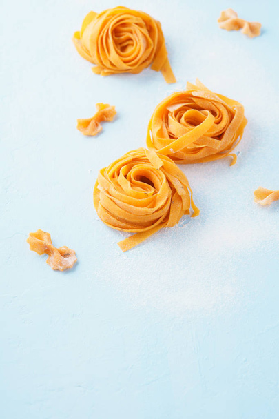 Italian pasta background. Uncooked fettuccine or tagliatelle and farfalle on light blue background. Empty space for text. - Valokuva, kuva