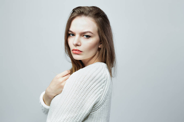 Gorgeous long-haired girl in a white knitted sweater is posing on the white background in the studio - Fotoğraf, Görsel