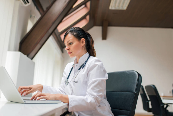 Side portrait of serious female doctor working on laptop. Close-up. - Foto, Imagen