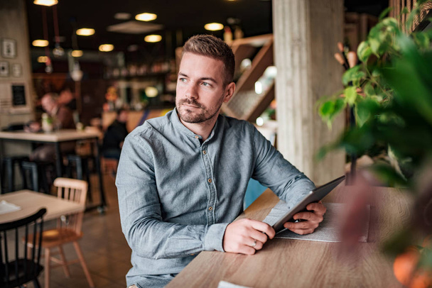 Portrait of a handsome entrepreneur with digital tablet in modern cafe. - Foto, afbeelding