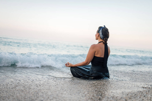 Young woman practicing yoga and meditating in the lotus position on the beach. - Valokuva, kuva