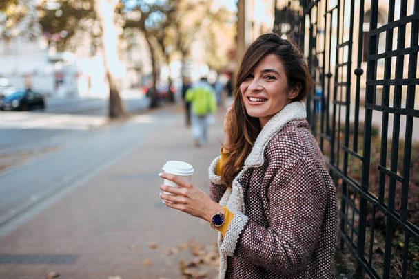 Портрет усміхненої молодої жінки, що тримає каву на винос
. - Фото, зображення