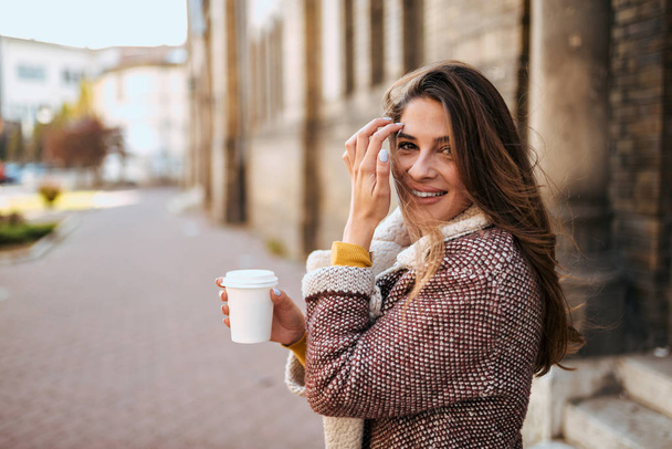 Gorgeous brunette walking in the city and drinking coffee. - Foto, imagen