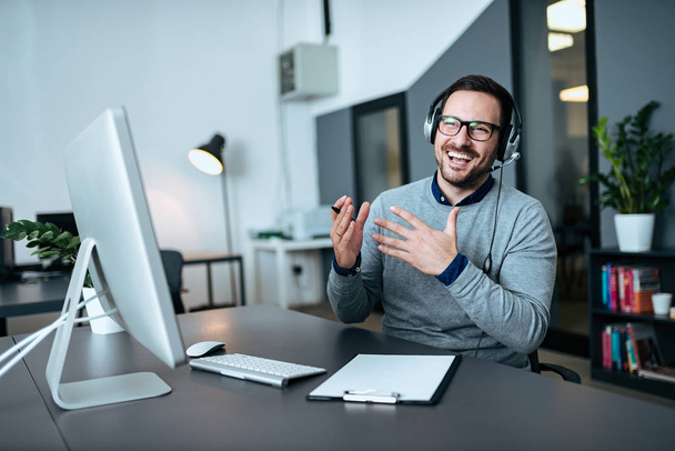 Happy young customer service operator talking via headset in modern office. - Фото, изображение