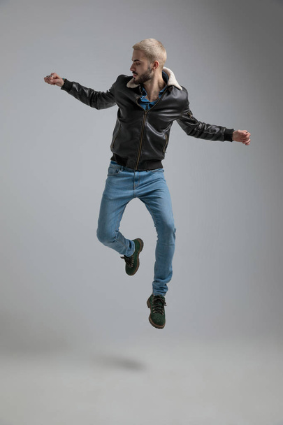 man in leren jas en jeans springen op grijze achtergrond - Foto, afbeelding