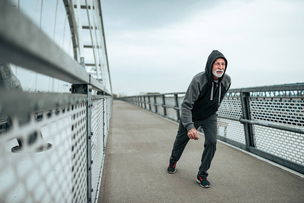 Fit male senior running across the bridge with his hood on. - Fotoğraf, Görsel