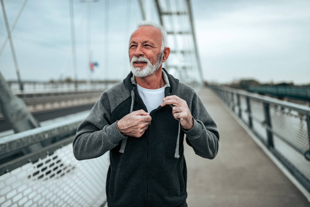 Portrait of a senior runner in a sportswear on the city bridge. - Фото, изображение
