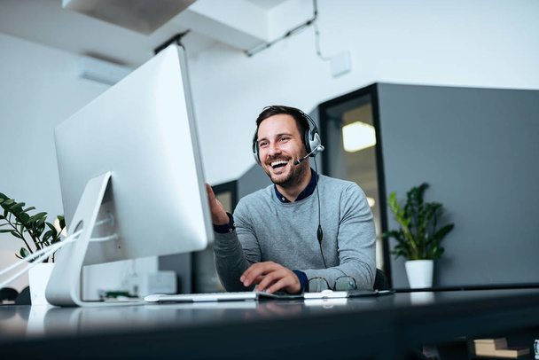 Low angle image of happy casual businessman working on computer with headset. - Photo, Image