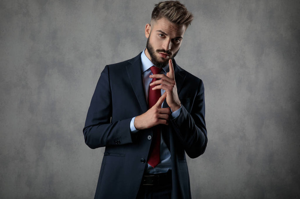 dramatic young businessman gesturing by rubbing his hands together on grey studio background - Photo, Image