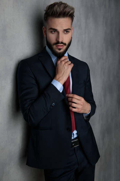 portrét sexy podnikatel drží jeho kravatu a vypadá daleko na šedou stěnu - Fotografie, Obrázek