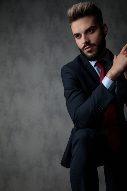 Porträt eines ernsthaften jungen Geschäftsmannes, der denkt und zur Seite schaut, während er die Handflächen auf grauem Studiohintergrund zusammenhält - Foto, Bild