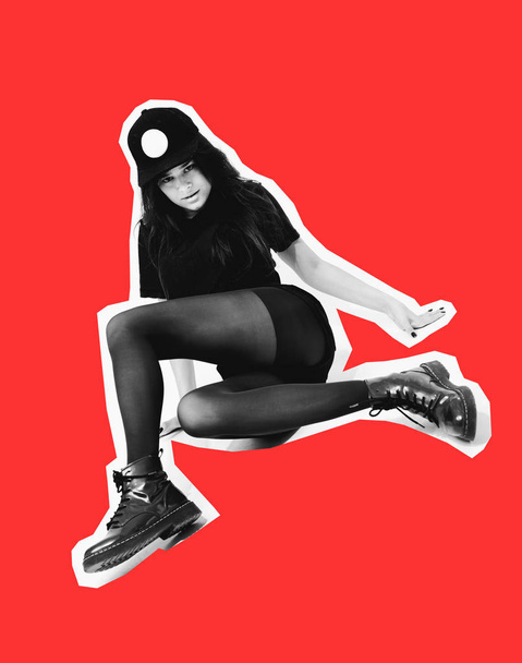 Stylish young dark-haired girl dressed in a black top, shorts, tights and cap poses sitting on the floor on the white background in the studio. Magazines collage style - Фото, зображення