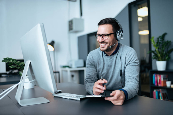 Portrait of a casual smiling businessman using headset when talking to customer. - Fotoğraf, Görsel