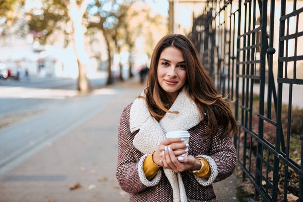 Urban portrait of stylish brunette holding take away coffee. - Zdjęcie, obraz