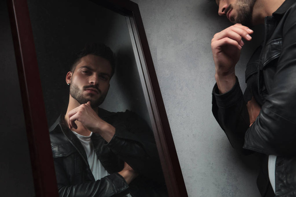 pensive young man looks in the mirror, studio picture - Фото, изображение