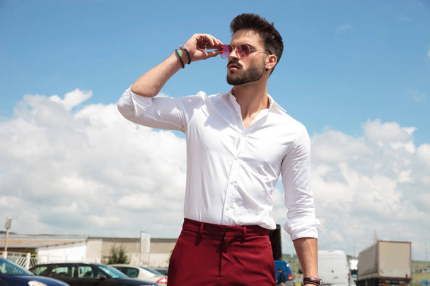 side view of attractive man fixing his glasses and walking in parking lot - Photo, Image