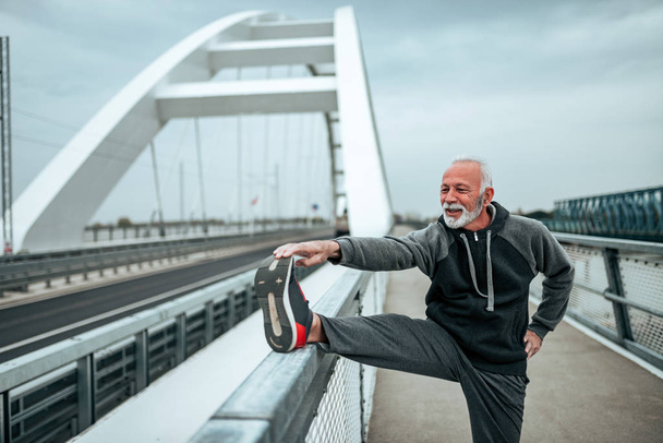 Senior sportsman stretching outdoors, on the city bridge. - Fotografie, Obrázek