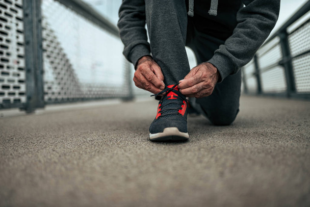Close-up image of senior man preparing for a run outdoors. Tying shoelaces. - Photo, Image