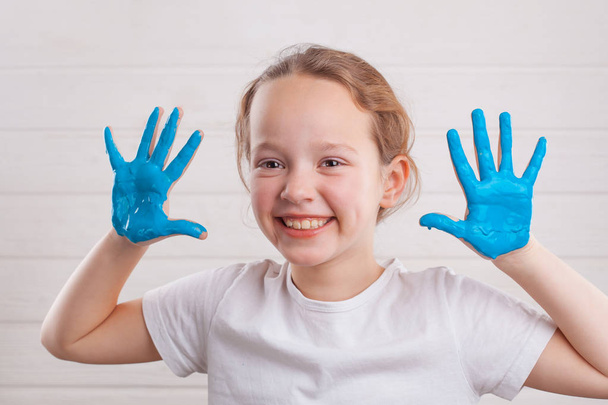 beautiful little girl with hands in the blue paint on the white wooden background - Фото, зображення
