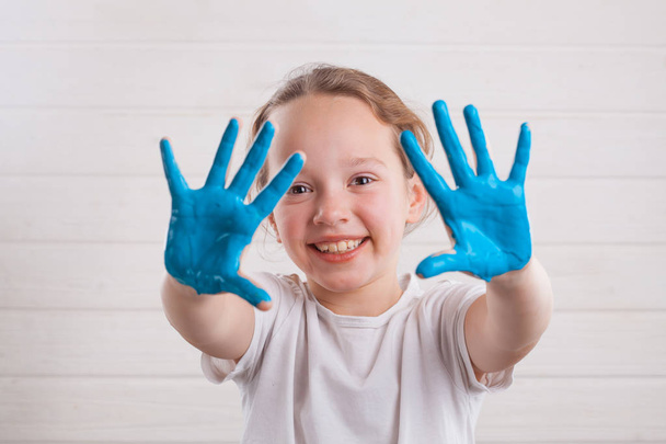 beautiful little girl with hands in the blue paint on the white wooden background - Valokuva, kuva