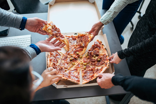 Close-up of a hands taking slices of pizza on a lunch break. - Fotografie, Obrázek