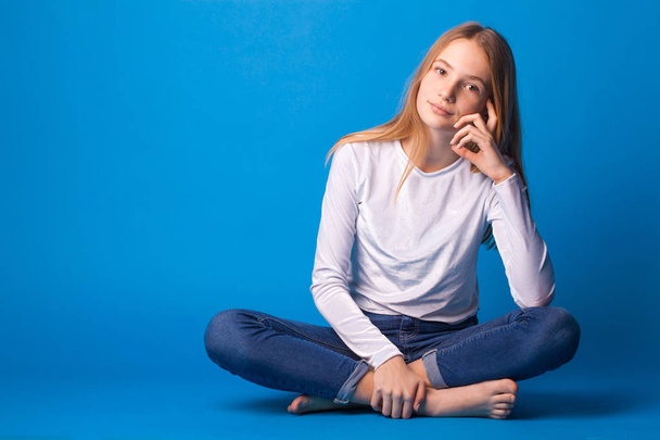 Beautiful smiling teen girl in jeans and a white blouse on blue background. - Photo, image