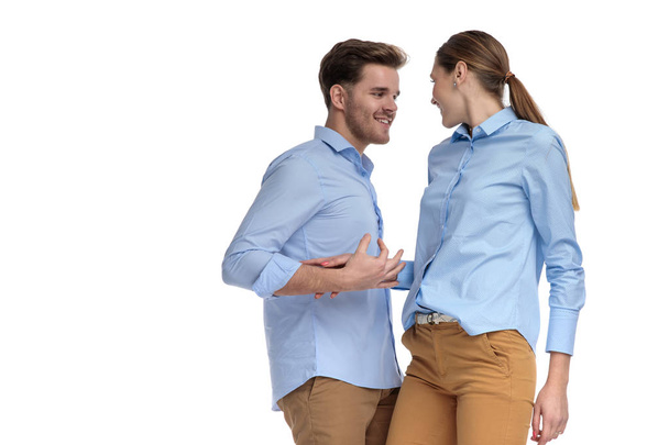 excited young casual couple looking at each other while standing on white background - Photo, Image