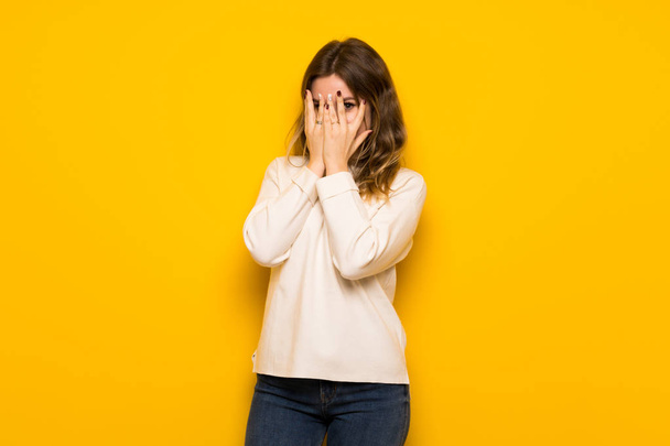 Teenager girl over yellow wall covering eyes by hands and looking through the fingers - Foto, Bild