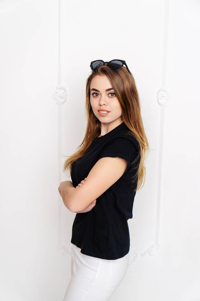 Retrato de uma rapariga num estúdio. Lindo rosto. T-shirt preta. Calças brancas
 - Foto, Imagem