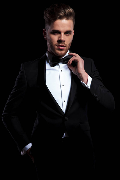 front view of young elegant man fixing his bowtie on black background - Photo, Image