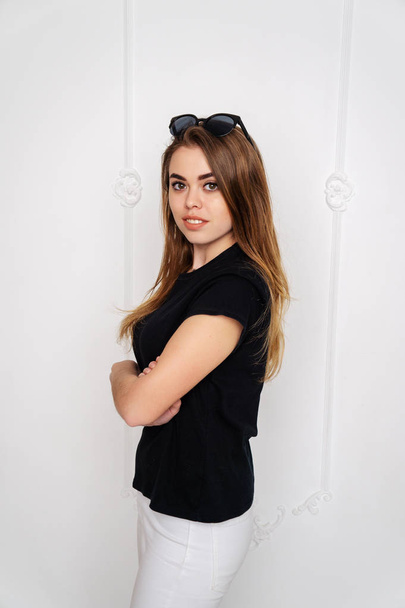 Portrait of a girl in a studio. Beautiful face. Black T-shirt. White pants - Foto, Imagen