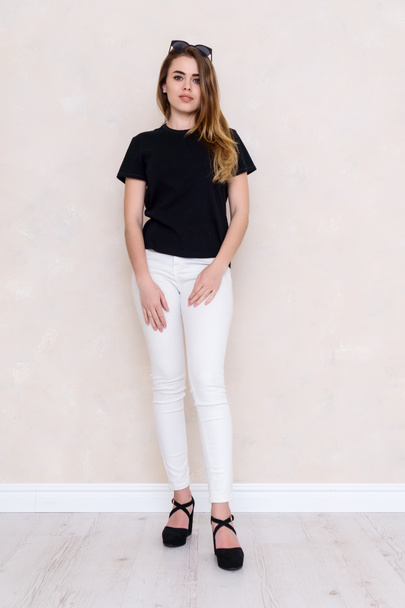 Πορτρέτο ενός κοριτσιού σε ένα στούντιο. Όμορφο πρόσωπο. Μαύρο T-shirt. Λευκό παντελόνι - Φωτογραφία, εικόνα