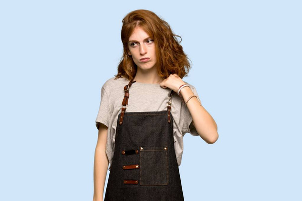 Young redhead woman with apron with a lot of heat over blue background - Photo, Image