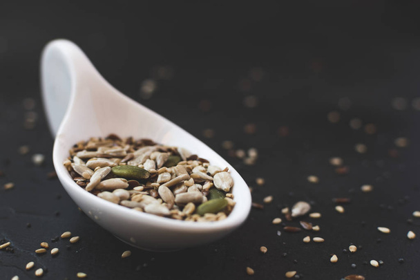 Sesame seeds next to different fruit seeds in a white ceramic spoon. Dark food concept - Photo, Image