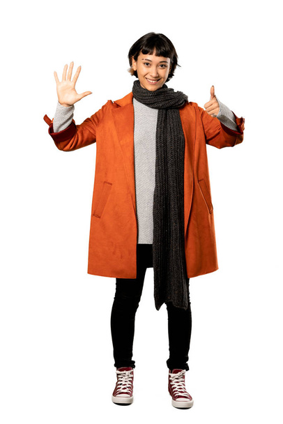 A full-length shot of a Short hair woman with coat counting six with fingers over isolated white background - Foto, Bild
