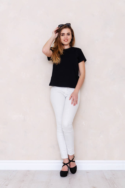 Portrait of a girl in a studio. Beautiful face. Black T-shirt. White pants - Fotó, kép