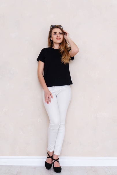 Portrait of a girl in a studio. Beautiful face. Black T-shirt. White pants - Foto, afbeelding